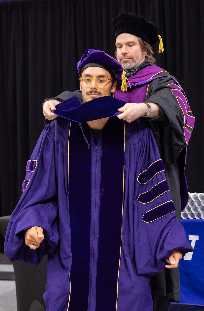 Will hoods Gian Marco at the Allen School graduation, standing in for his advisor Armita Nourmohammad (now at Yale).